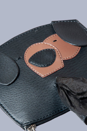 Close up Front view of Boboli poo bag holder. Cute dog face shaped poo waste bag holder with dispenser hole at the mouth position on the front with bag emerging.. Gold clasp doubles as wide zip feature at bottom of the bag holder